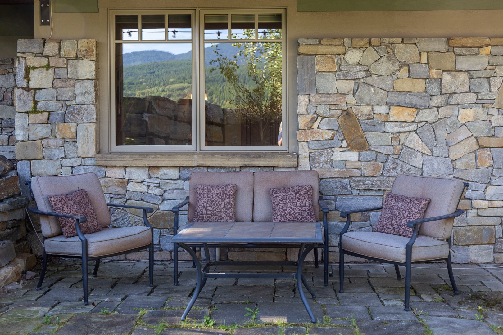 The patio invites quiet conversations with mountain scenery framed through the windows, cushioned seating waiting beneath the stone facade for your morning coffee or evening wine.