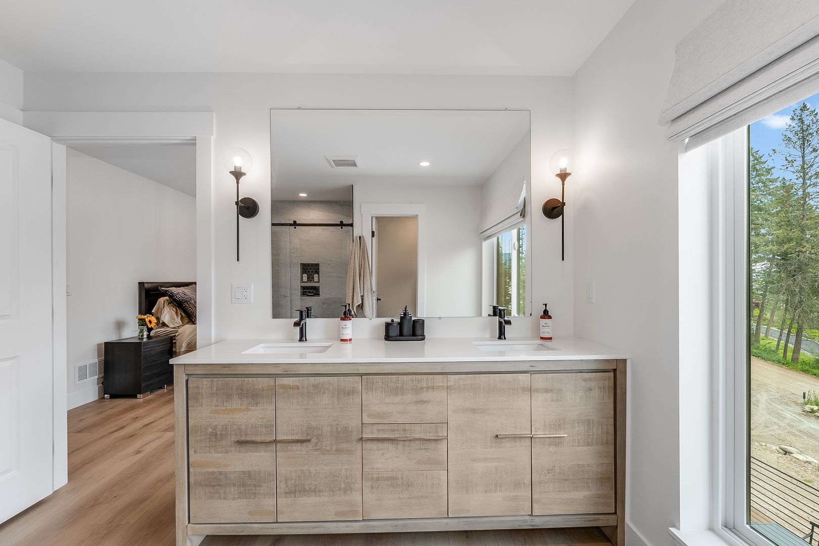Your spa-like bathroom features a spacious double vanity with modern fixtures, elegant sconces, and natural light streaming through the window, creating a serene space to start each morning refreshed.