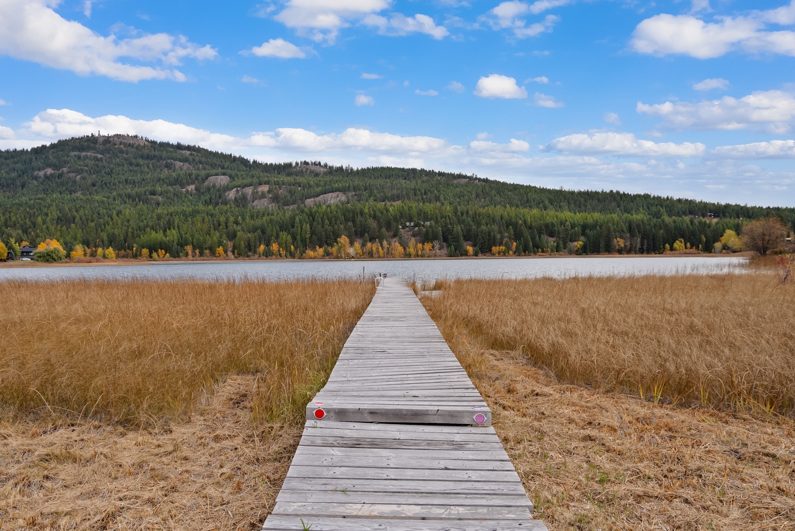 Serene lakeside setting with wooden dock extending into calm waters, surrounded by golden autumn foliage and forested hills.