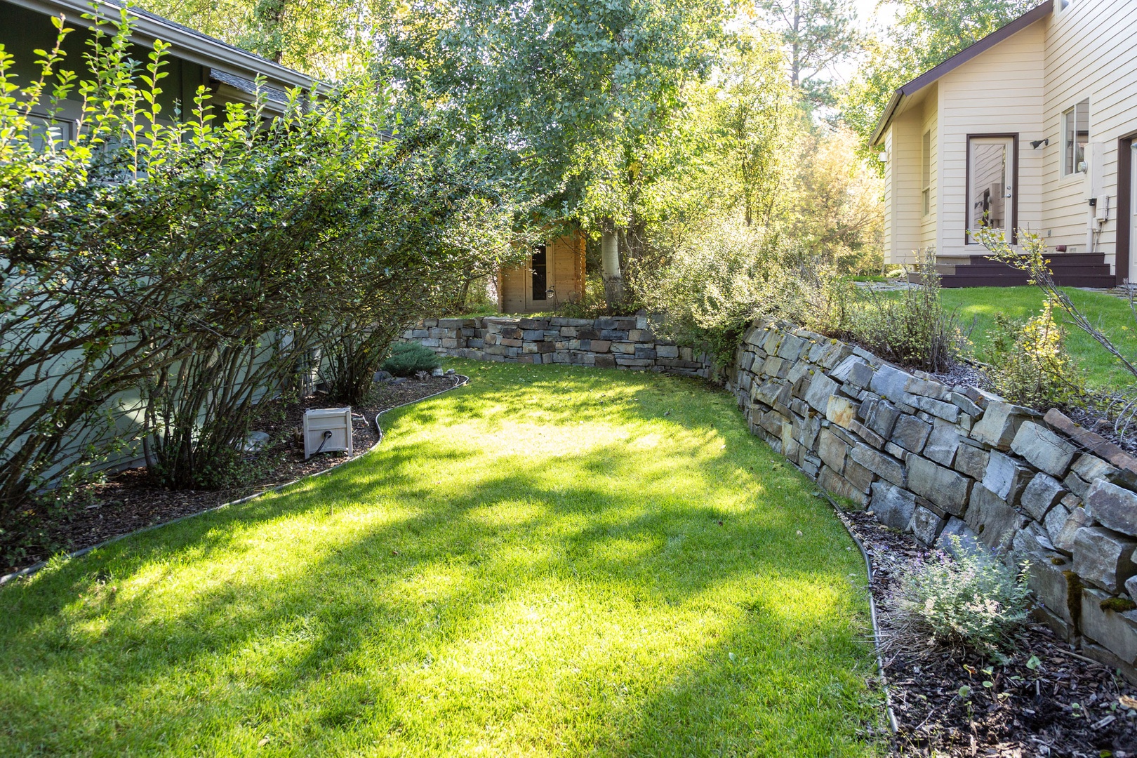 A peaceful courtyard garden with lush green grass, natural stone walls, and sheltering trees creates a private outdoor retreat for relaxation and quiet moments.