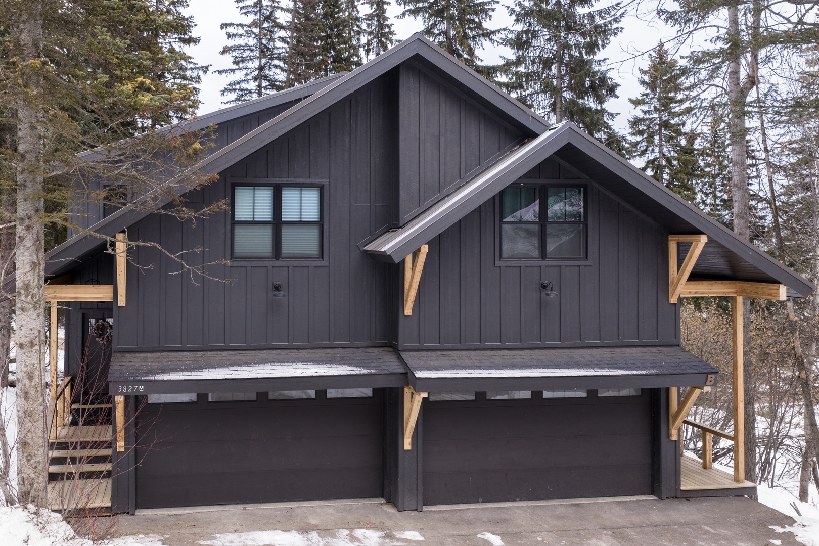 Modern mountain cabin featuring dark wood siding with natural wood accents, nestled among towering evergreens in a peaceful wooded setting.