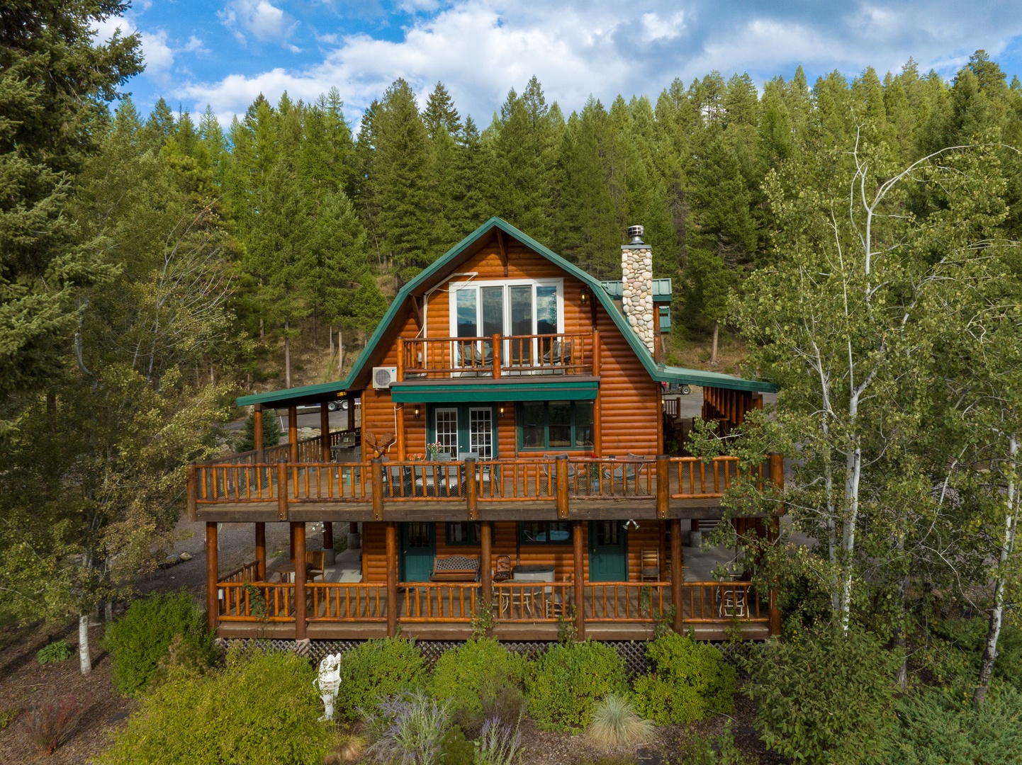 A stunning log cabin with spacious decks nestled into a forested hillside, offering a peaceful mountain retreat surrounded by towering pines and natural beauty.