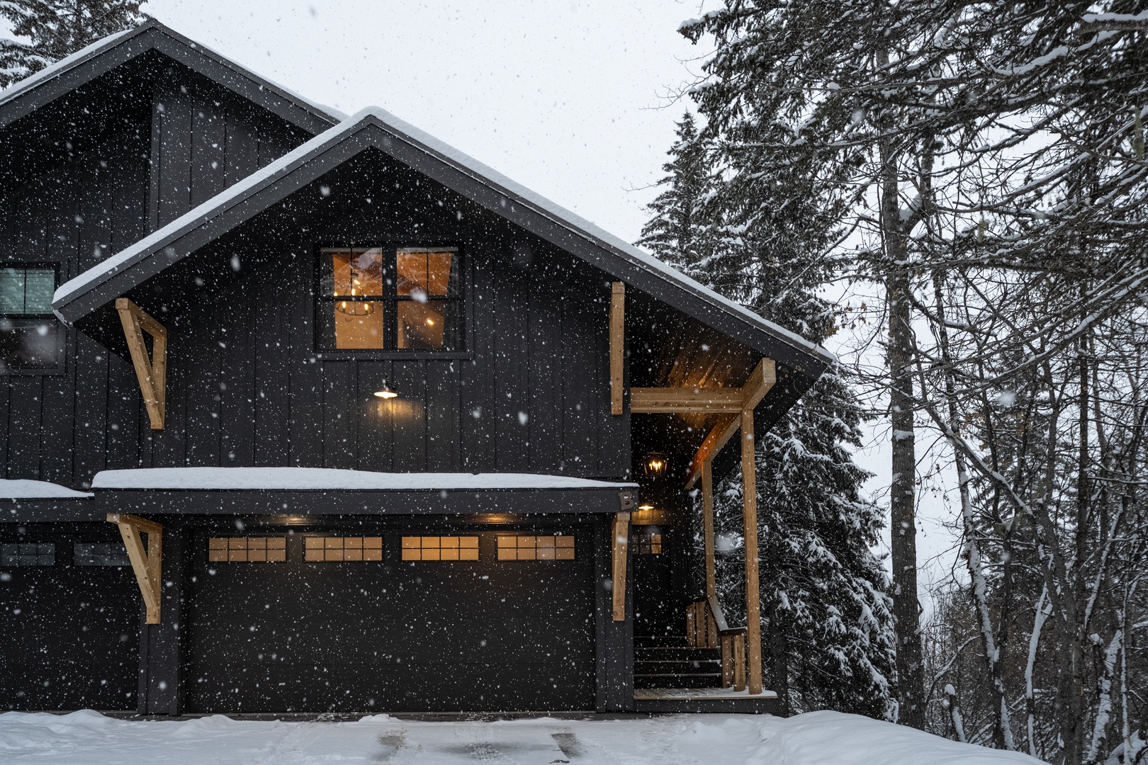 Snow falls gently around this cozy mountain retreat, where warm lights glow through frosted windows and evergreens stand guard in winter's embrace.