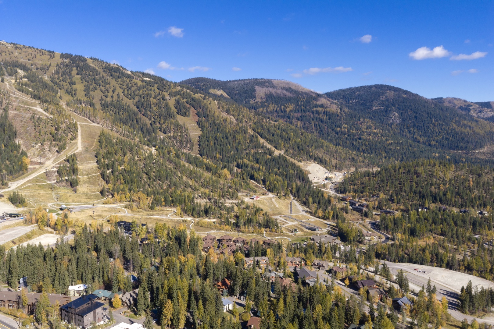 Aerial view of a mountain resort area nestled among forested peaks and winding roads, capturing the natural beauty of the surrounding landscape and access routes.