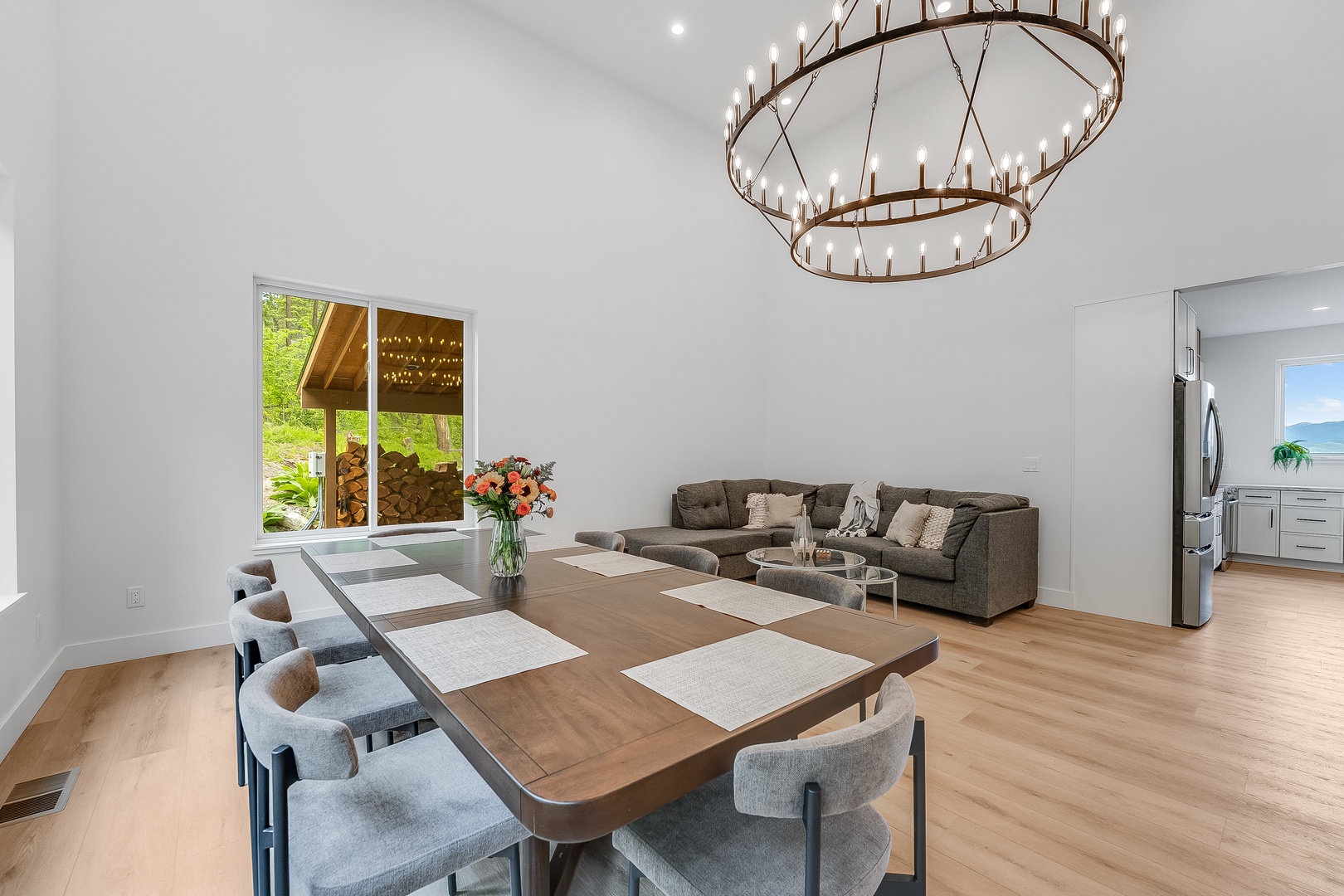 Your open dining and living space features high vaulted ceilings, a striking chandelier, and natural light streaming through large windows. Gather around the stylish dining table or unwind on the cozy sofa.