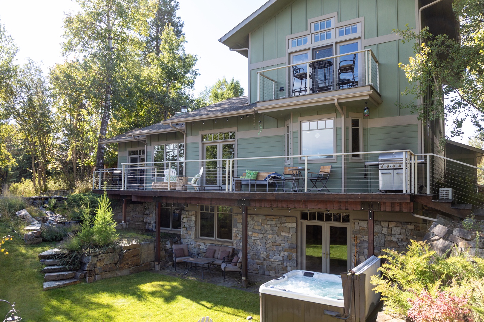 A modern mountain home with multiple decks, outdoor entertaining space, and a relaxing hot tub nestled in a lush, tree-lined setting.