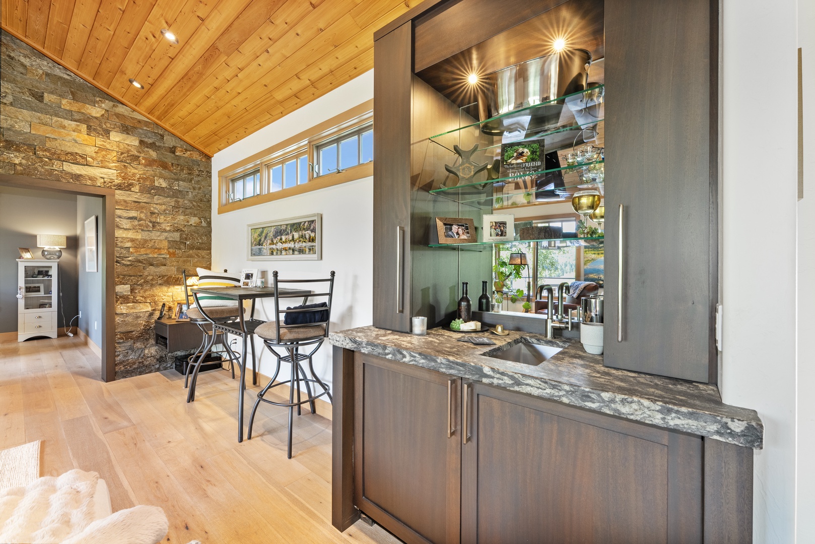 Step into your open-concept retreat, where rustic stone walls meet soaring wood ceilings. The sleek bar and cozy dining nook invite you to unwind in warmth and style.