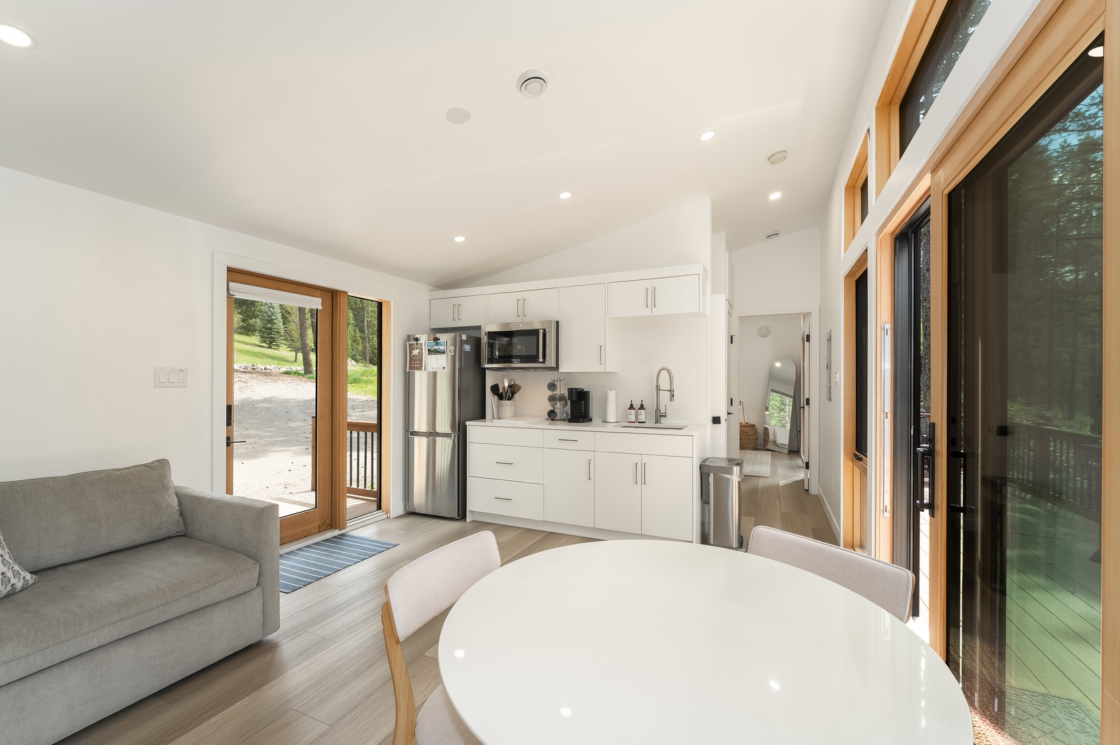 Imagine preparing your morning coffee in this bright, open-concept space where the kitchen flows seamlessly into the living and dining area, bathed in natural light from those beautiful wood-framed glass doors.