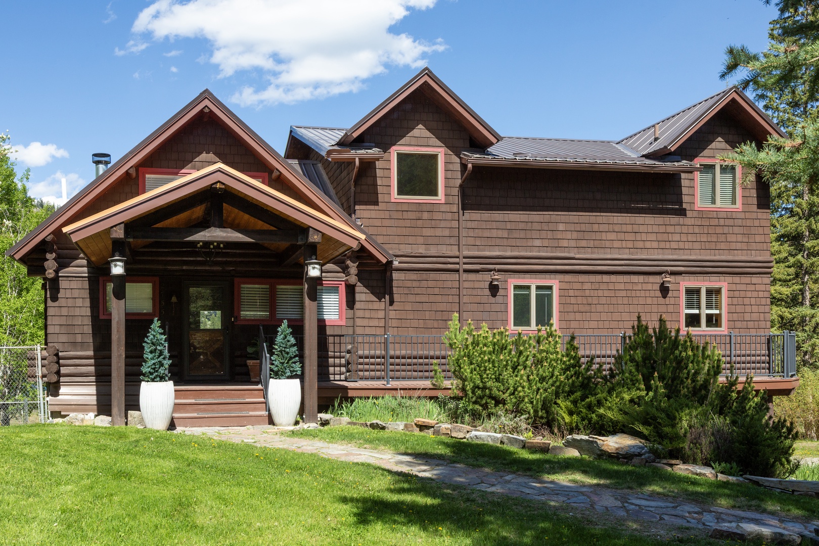 A charming mountain lodge with a welcoming covered entrance, rustic wood siding, and multiple gabled rooflines set against a backdrop of blue skies and surrounding natural beauty.
