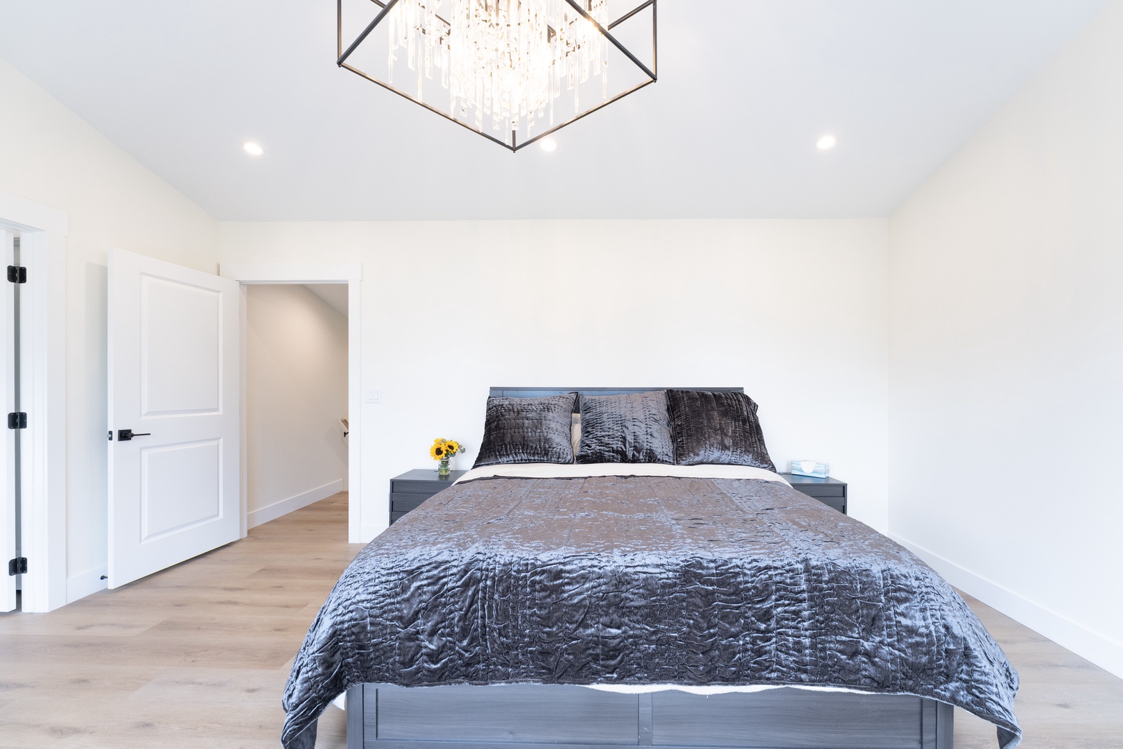 Sink into plush bedding beneath a stunning statement chandelier in your serene retreat, where vaulted ceilings and soft lighting create a peaceful escape.