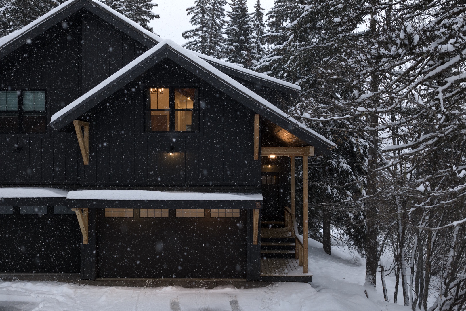 Mountain cabin nestled among snow-laden evergreens, with warm lights glowing through windows as fresh powder falls gently outside.