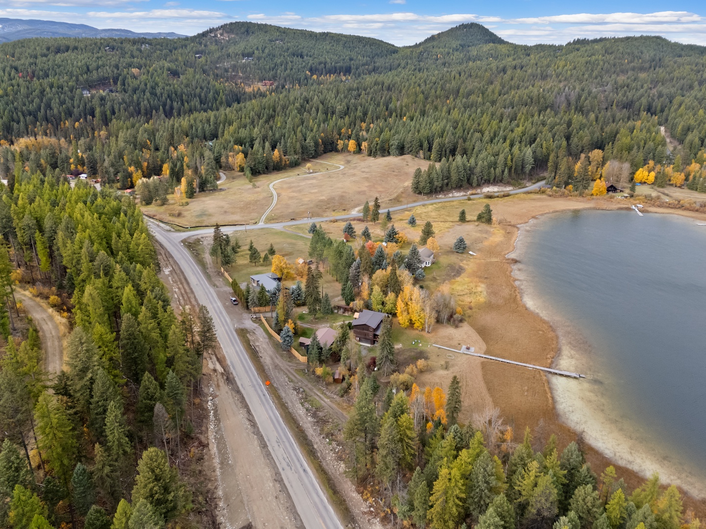 Stunning aerial view of lakeside property nestled among forested mountains with vibrant autumn foliage and peaceful waterfront setting.