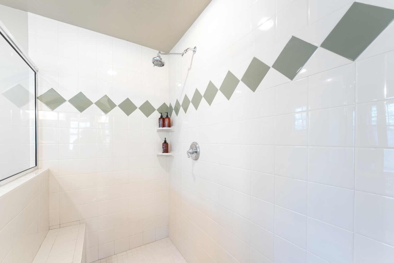 Step into a bright, modern shower featuring gleaming white tile with a playful geometric accent. Enjoy a refreshing rinse under the rainfall head, with natural light streaming in and built-in shelves for your essentials.