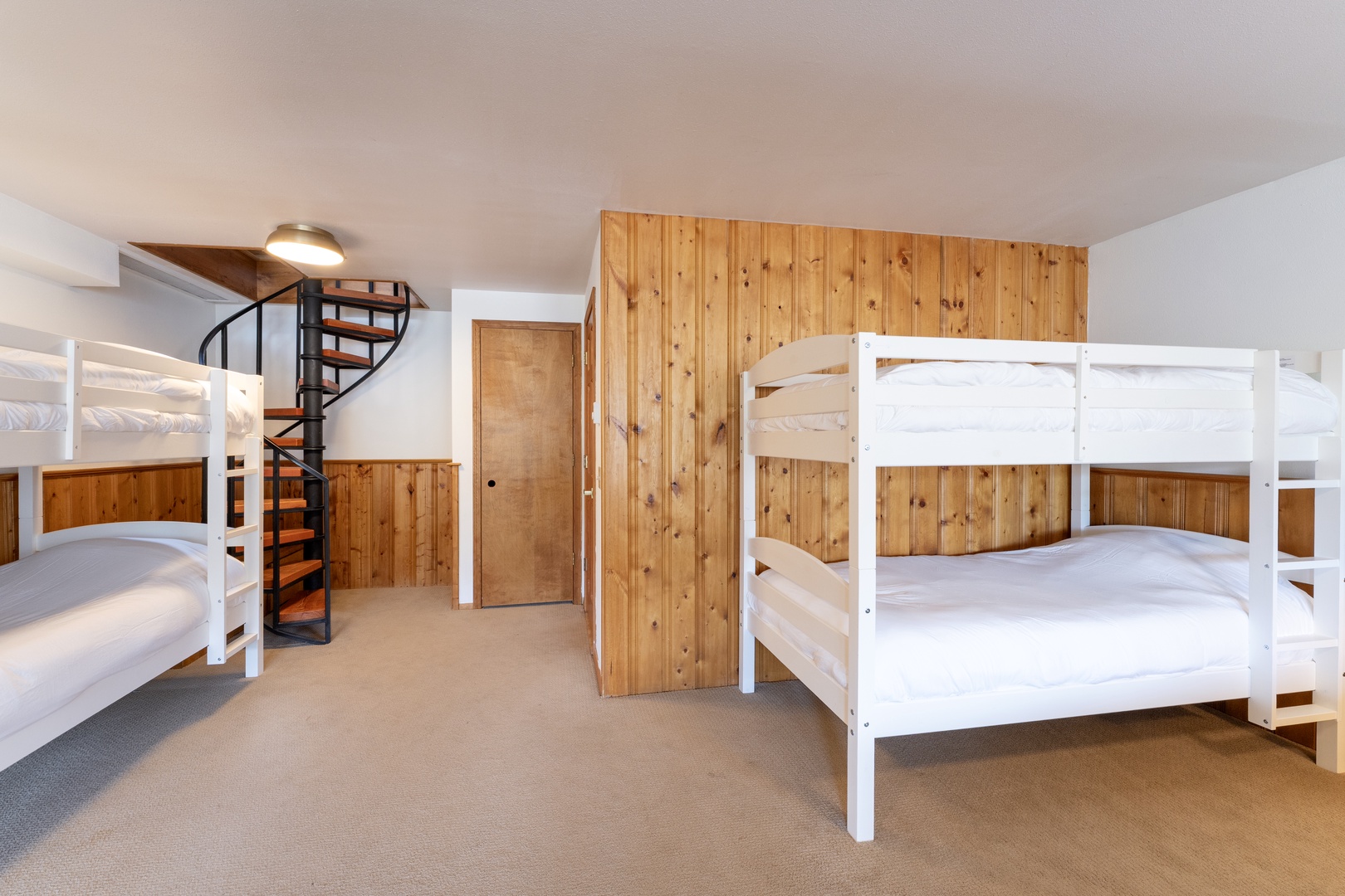 Your spacious bunk room features comfortable beds with crisp white linens, warm wood paneling, and a charming spiral staircase.