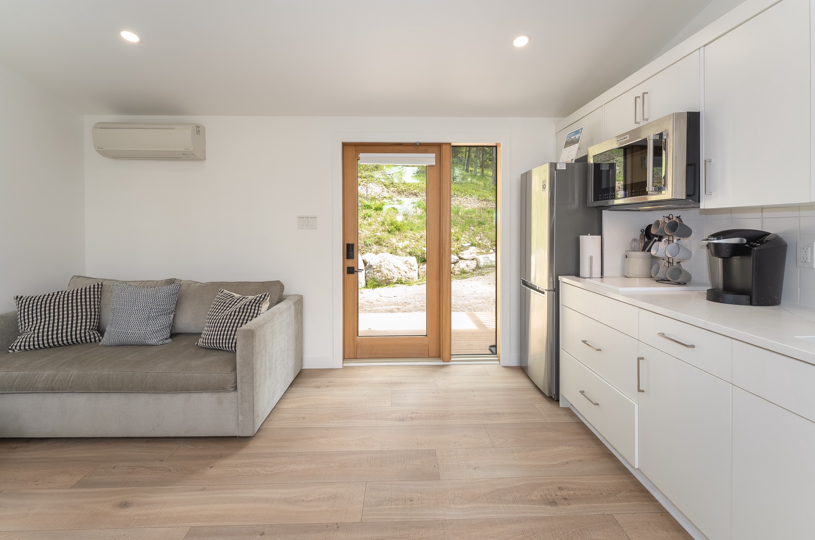 Unwind on the plush sofa or whip up a meal in your modern kitchenette—complete with stainless appliances, coffeemaker, and sleek white cabinetry. Climate-controlled comfort and a door to nature await.