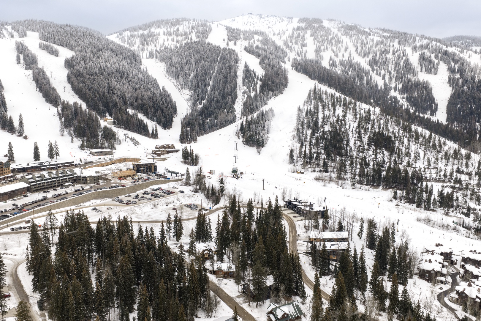 Spectacular ski resort nestled among snow-covered mountains with multiple ski runs, base lodge facilities, and parking areas.