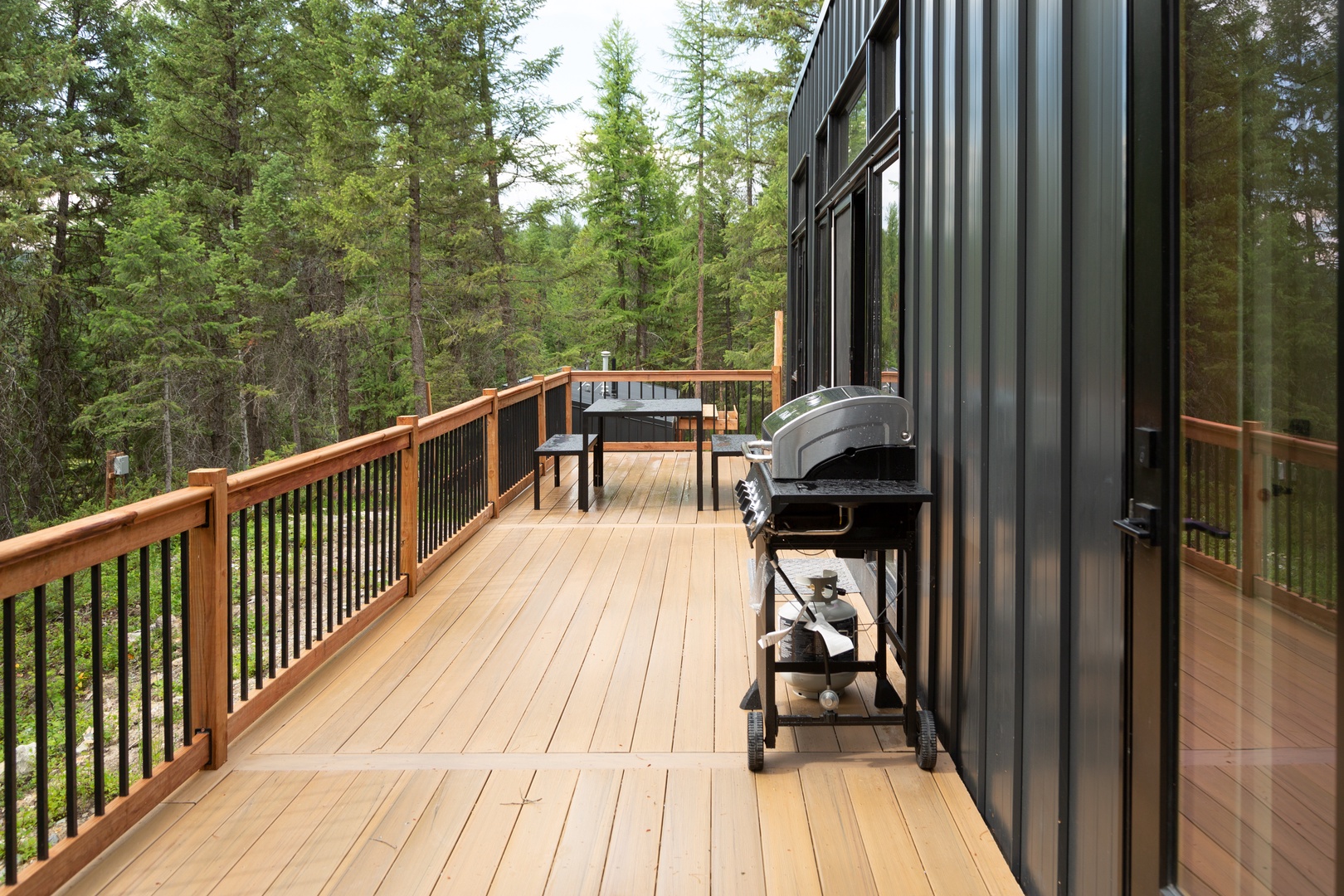 A spacious wooden deck equipped with a grill and dining table, surrounded by towering pines and serene forest views—perfect for your outdoor meals and relaxation.