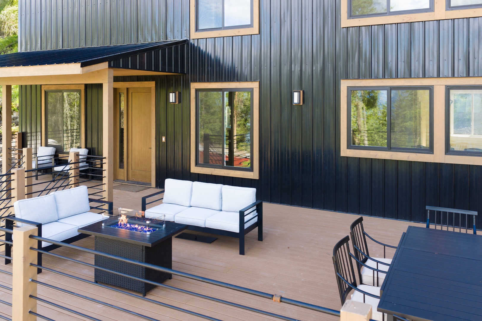 Modern vacation home with spacious deck featuring comfortable outdoor seating and a fire table—perfect for gathering, relaxing, and enjoying the fresh air surrounded by nature.