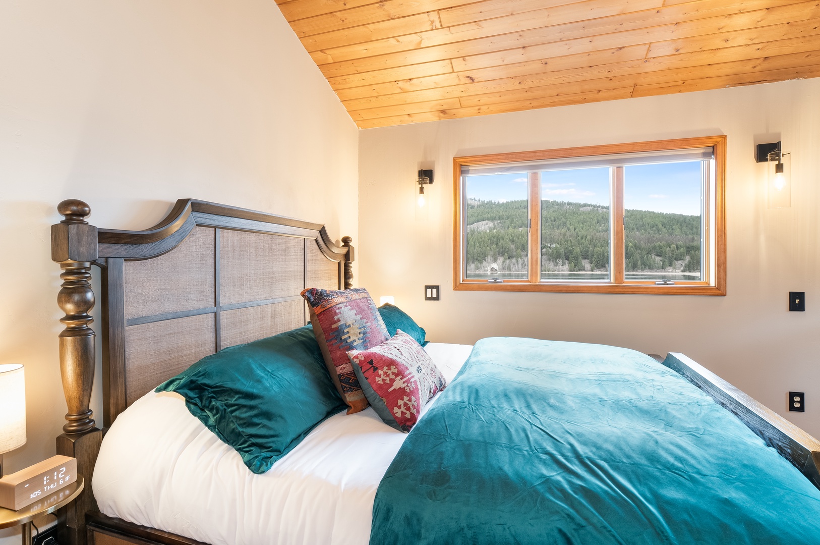 Wake up to stunning forest views from your cozy bed, wrapped in luxurious teal bedding under warm wood beam ceilings.