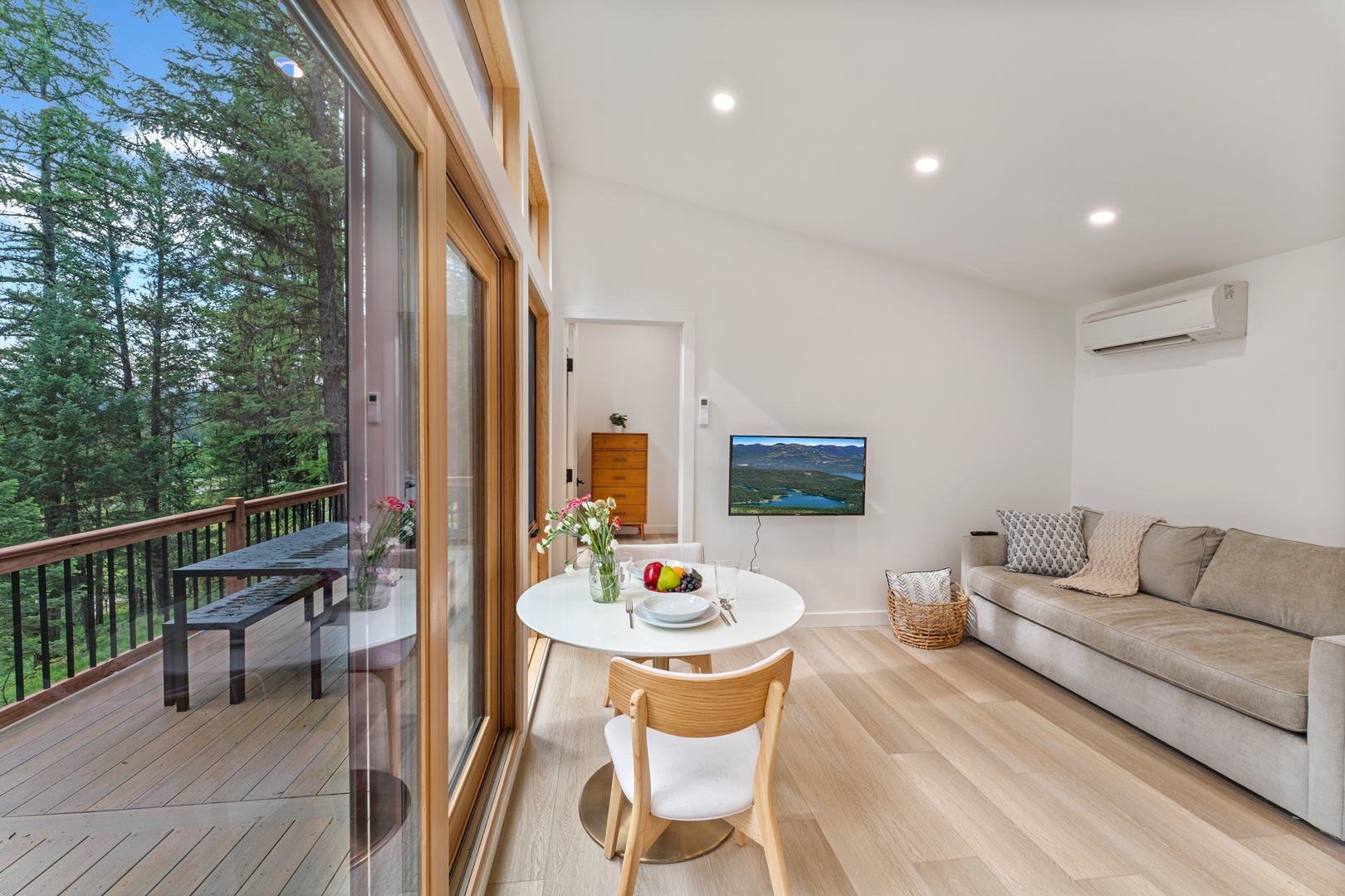 Step into your bright, modern living space where floor-to-ceiling windows frame lush forest views. Relax on the comfortable sofa, enjoy meals at the charming bistro table, and unwind on your private balcony surrounded by nature.