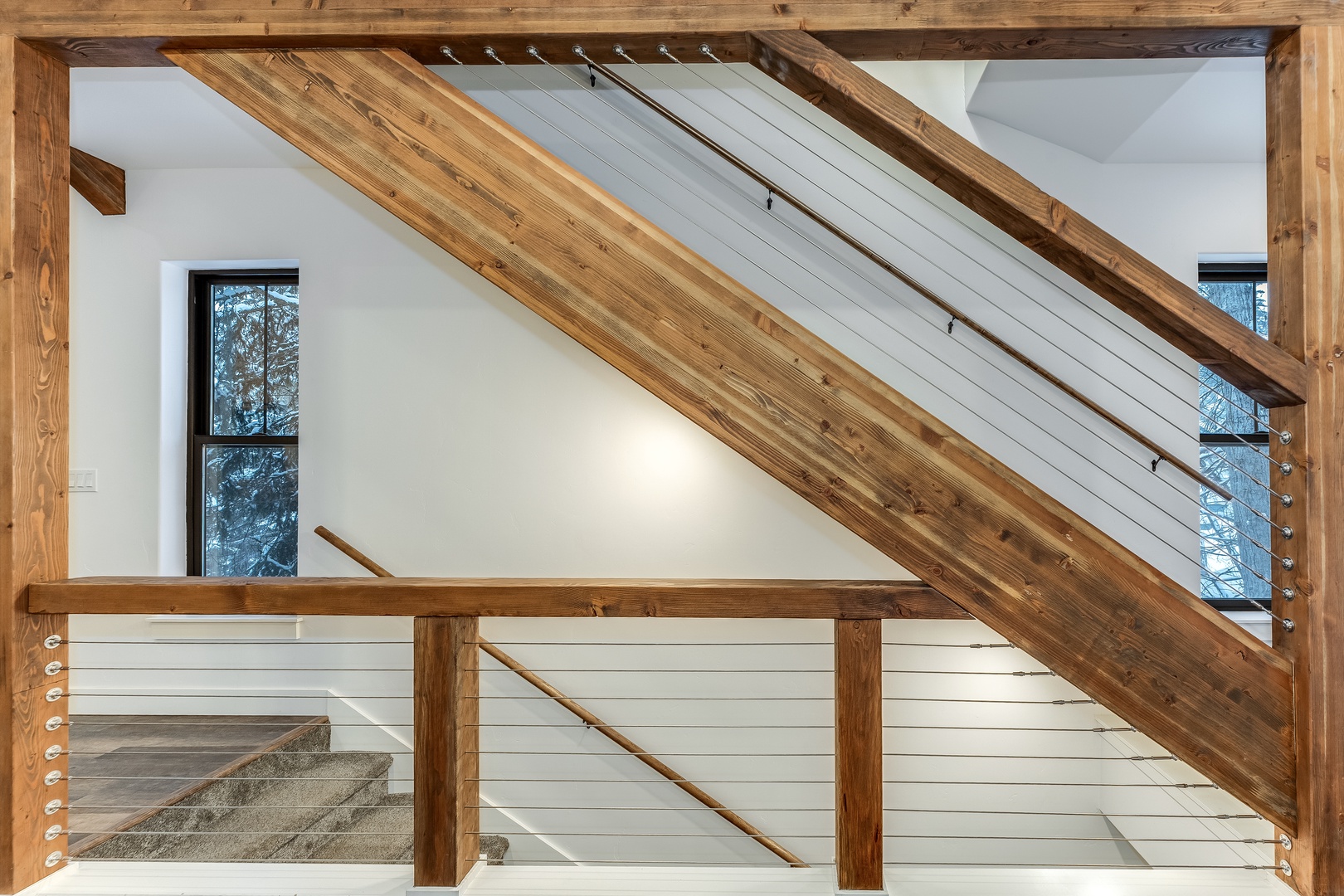 Experience modern mountain elegance as you ascend these stunning wooden stairs with sleek cable railings and forest views.