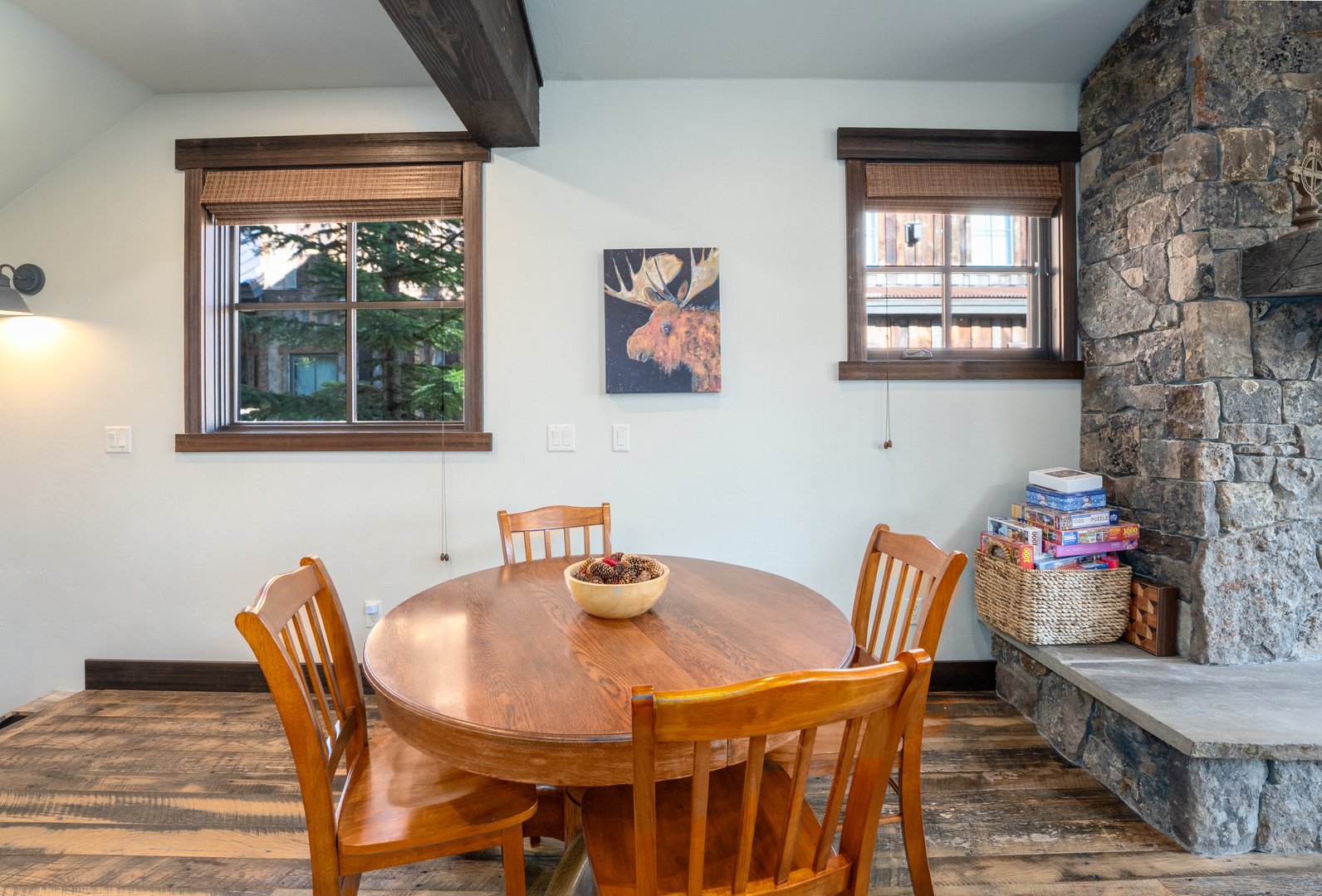 Gather around the warm wooden table with loved ones, where rustic beams and a stunning stone fireplace create a cozy mountain retreat atmosphere perfect for your morning coffee or evening games.