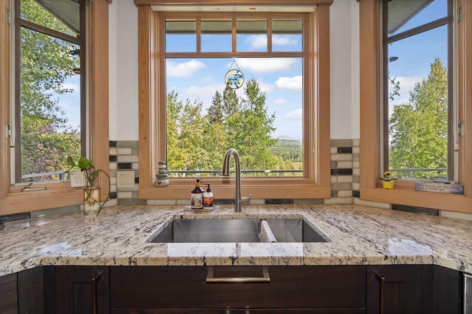 Prepare meals at your modern kitchen sink while taking in sweeping views of forested hills through expansive windows that flood the space with natural light.