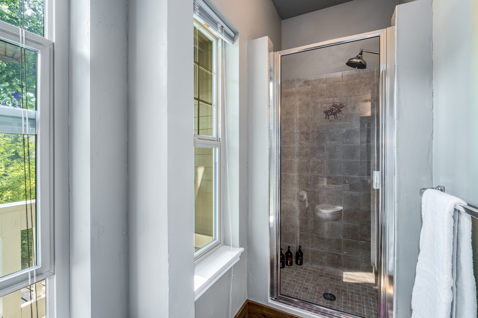 Step into your private spa-like retreat, where natural light pours through tall windows and a spacious walk-in shower awaits, complete with a refreshing rainfall head and elegant tilework.
