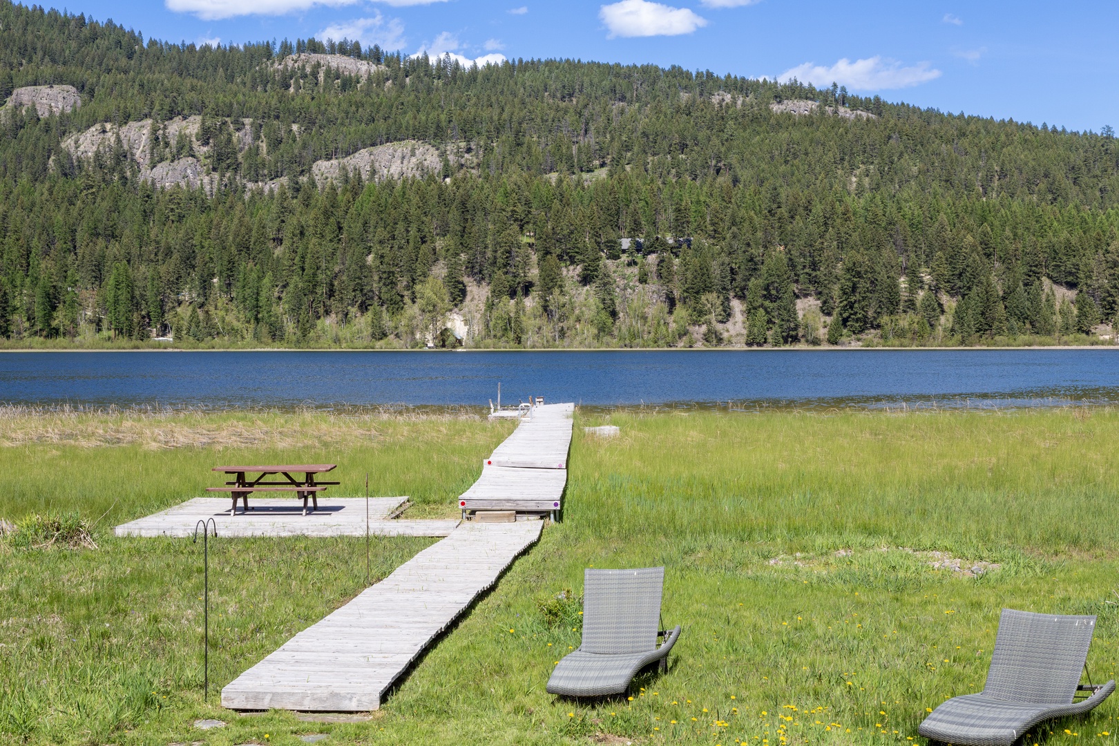 Peaceful lakeside setting with private dock and loungers, backed by forested mountain slopes—a serene retreat for your vacation stay.