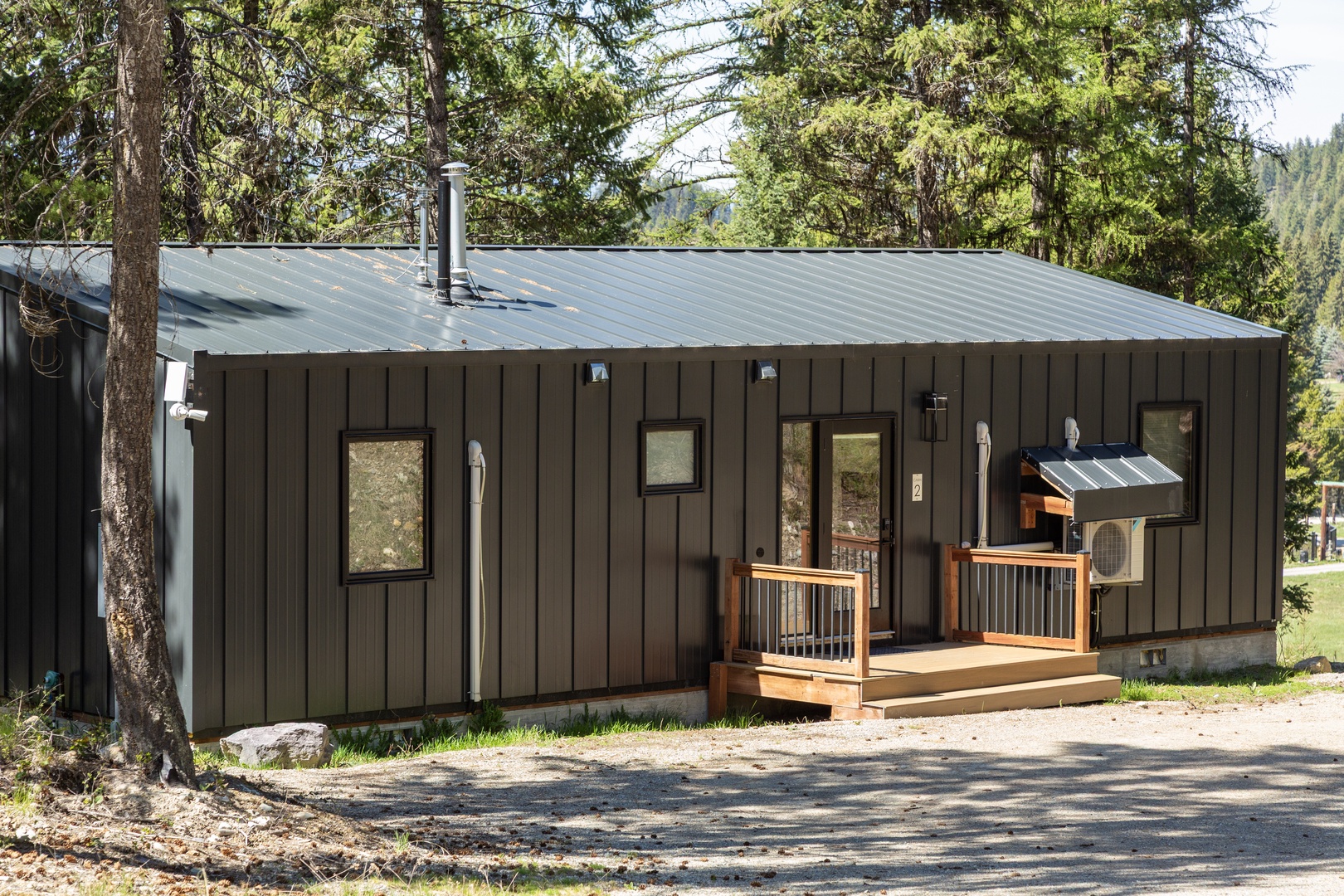 A charming rustic retreat nestled among towering pines with modern metal siding, a welcoming front deck, and peaceful forest surroundings.