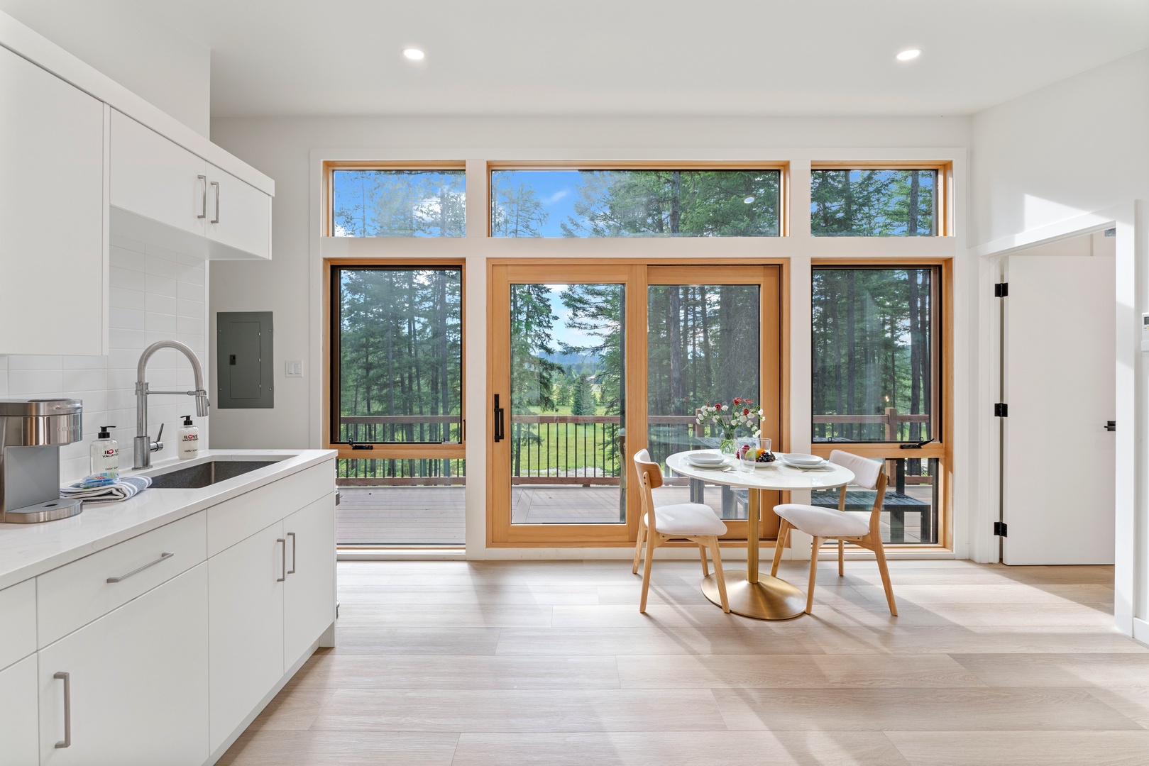 Your bright kitchen flows seamlessly to the dining area, where forest views through floor-to-ceiling windows create a serene backdrop for meals.