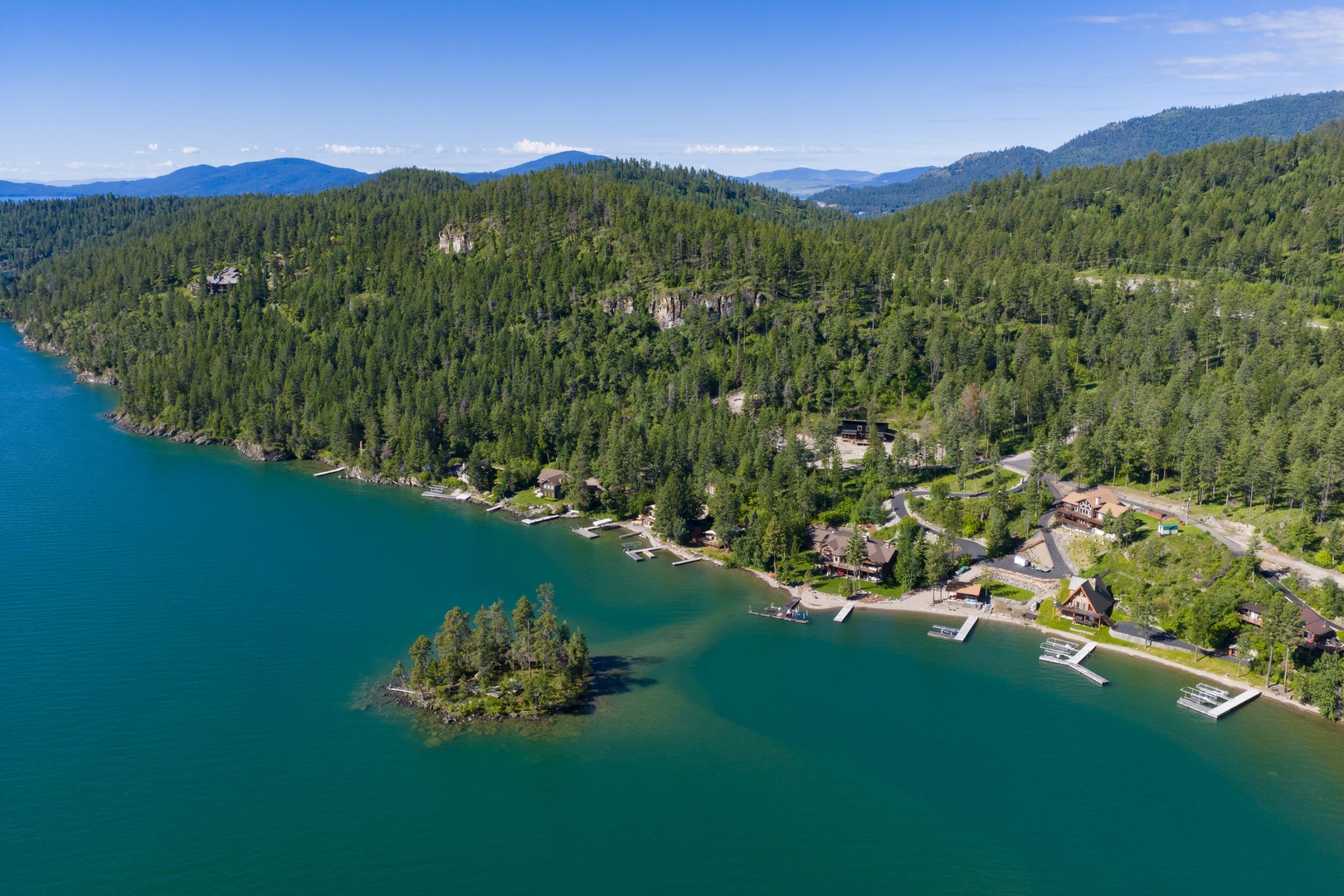 Aerial view of the lakefront property nestled among forested mountains with private boat docks along pristine turquoise water.