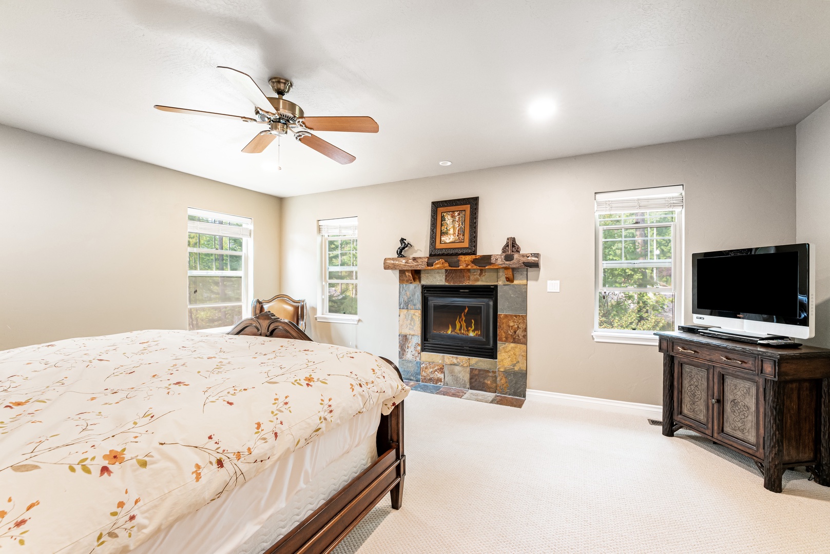 Relax in your spacious retreat featuring a cozy stone fireplace and natural light streaming through multiple windows, inviting you to unwind and feel right at home.