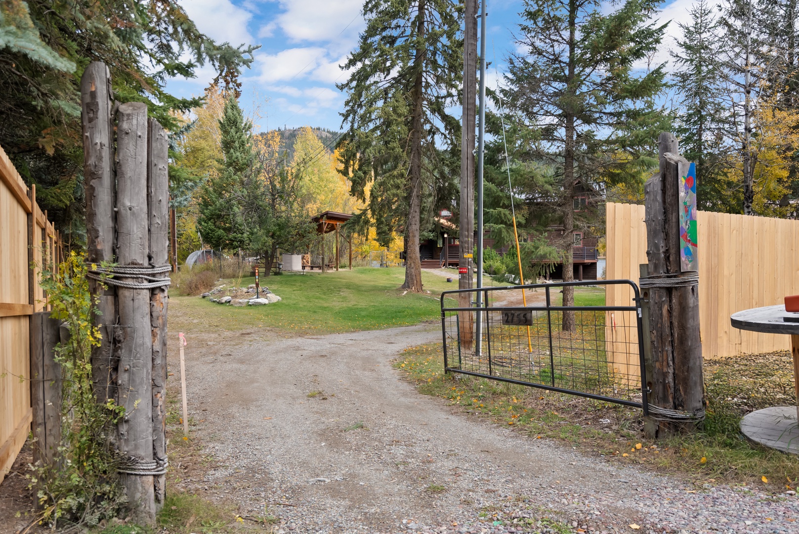 Property entrance gate opens to wooded grounds with mature evergreens and autumn foliage creating a peaceful mountain setting.