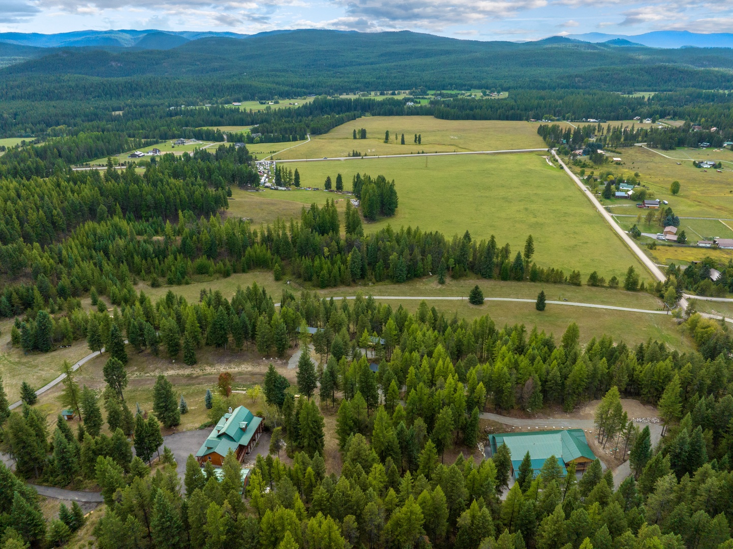 Aerial view showcases the property nestled among dense forests with rolling mountain ranges stretching across the horizon.