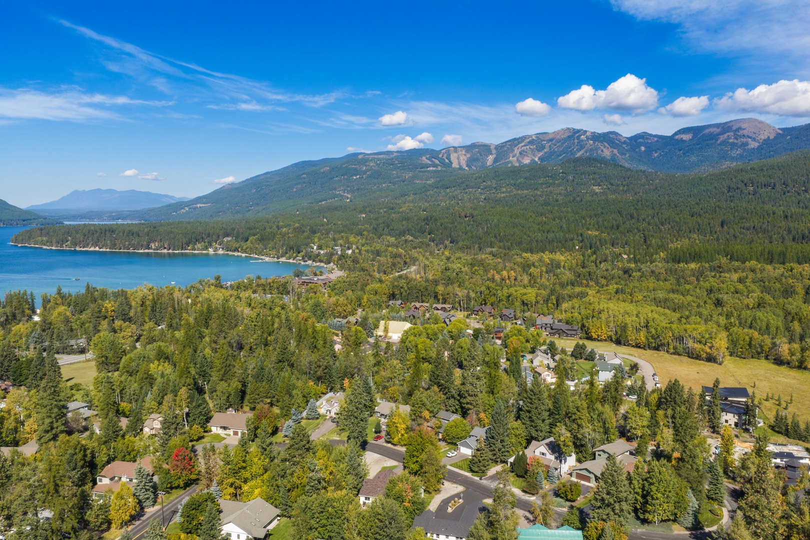 A forested lakeside community sits nestled between turquoise waters and soaring mountain peaks, surrounded by natural beauty and tranquil landscapes.