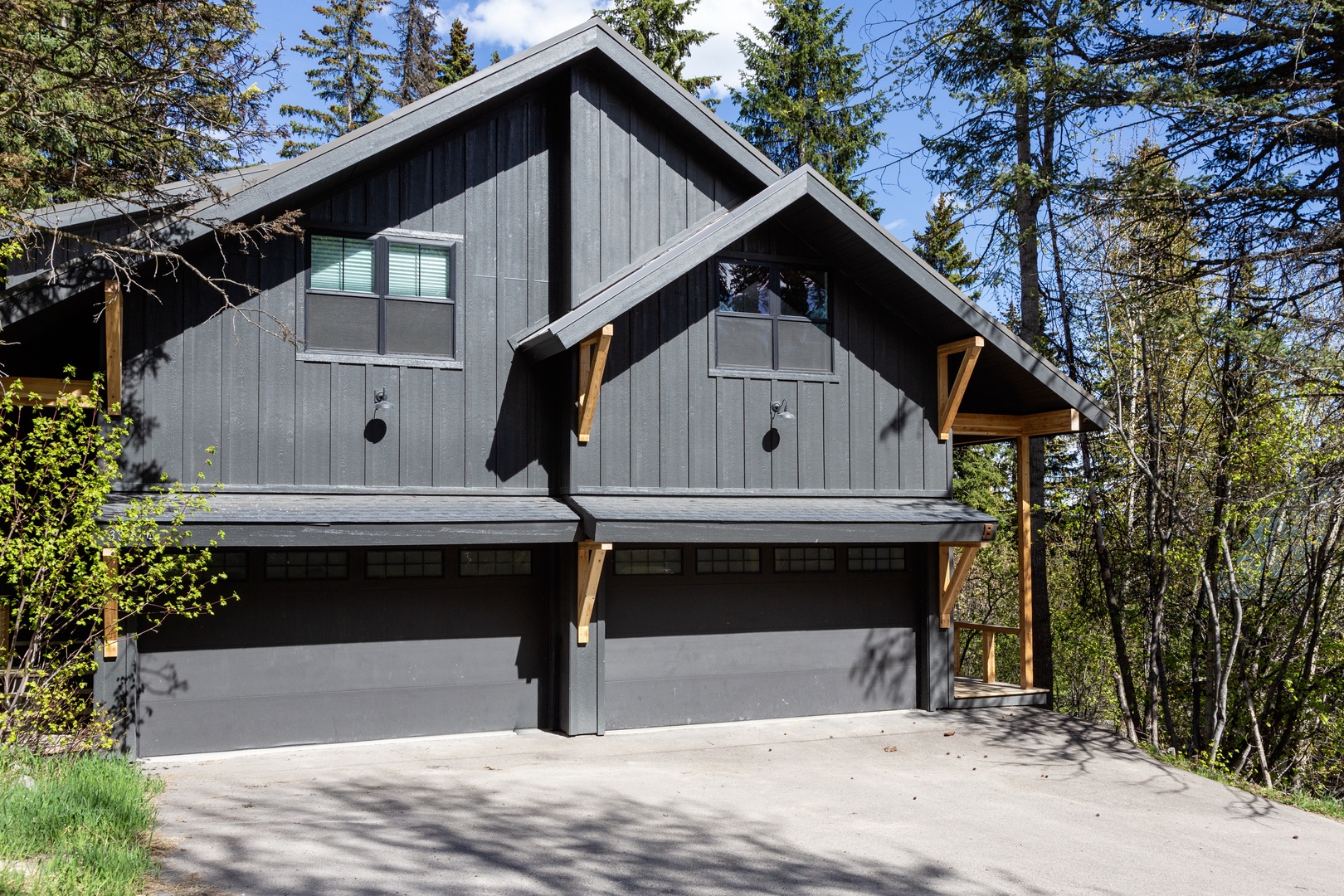 Modern mountain retreat nestled among towering pines, featuring distinctive dark wood siding, covered entry, and ample parking for your mountain getaway.