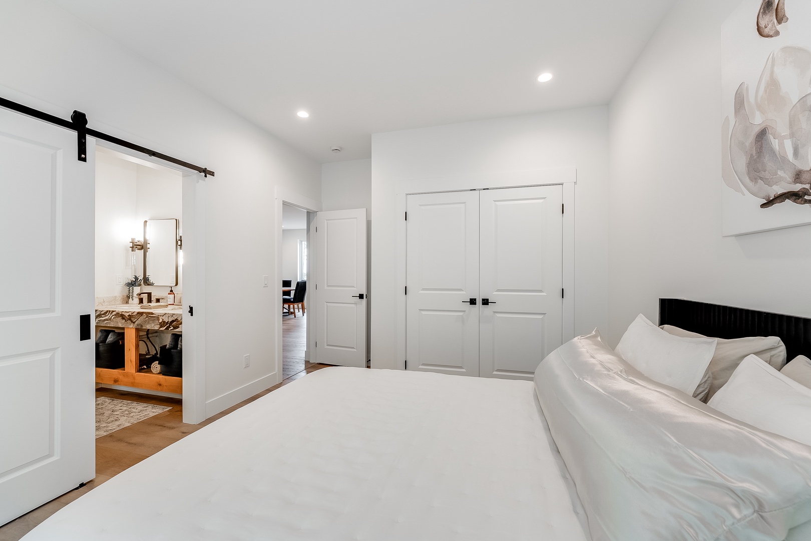 Your serene suite features crisp linens, elegant barn door access to the private bath, and peaceful white tones that invite you to unwind after exploring.