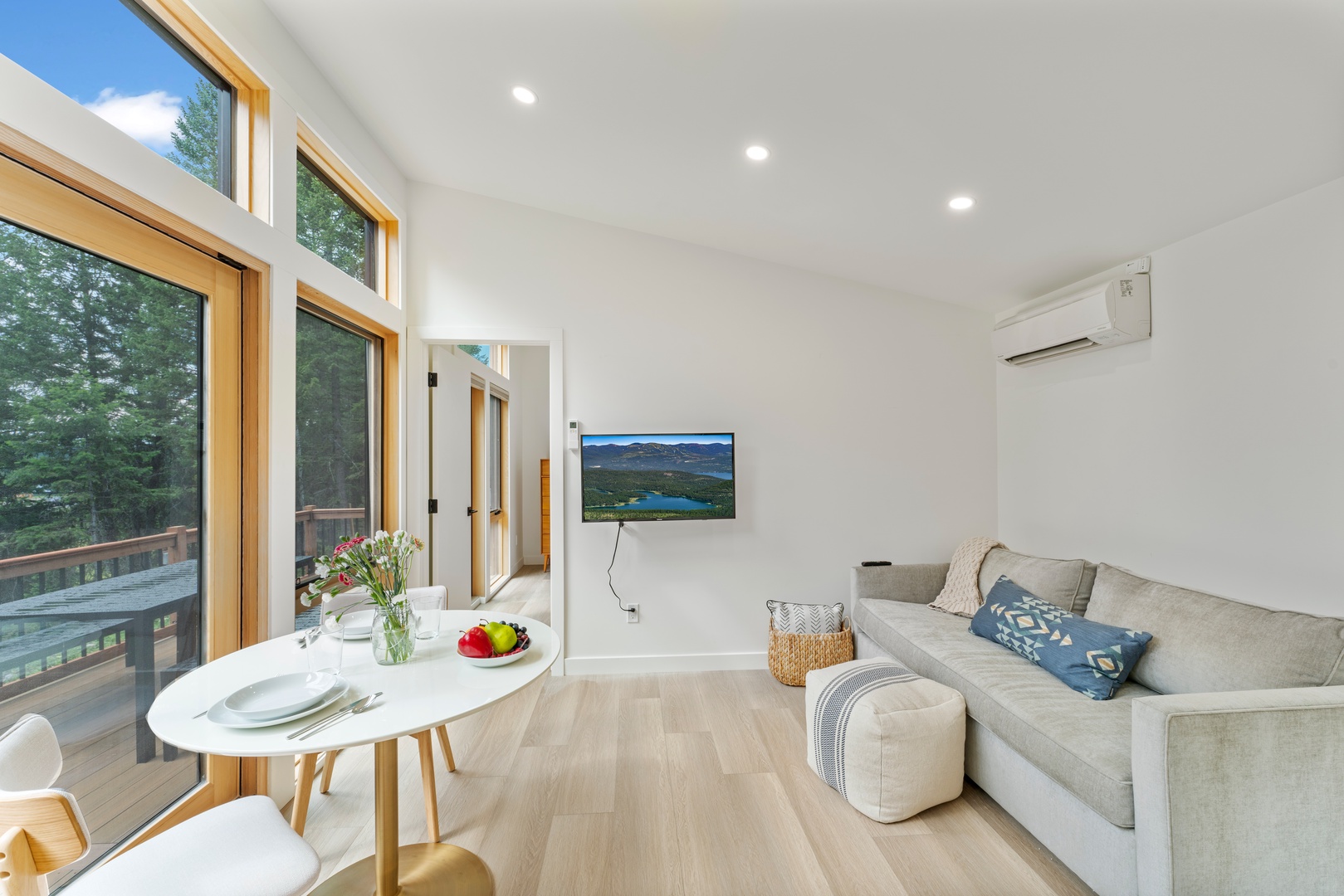 Your bright, open living space invites relaxation with a cozy sofa, flat-screen TV, and large windows framing forest views, all cooled by air conditioning.