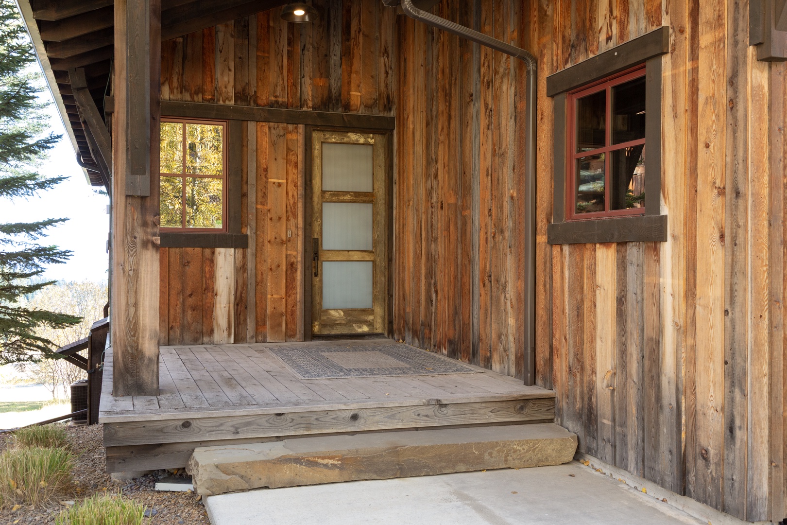 This rustic cabin entrance welcomes you with warm reclaimed wood siding and a charming covered porch, surrounded by peaceful natural beauty.