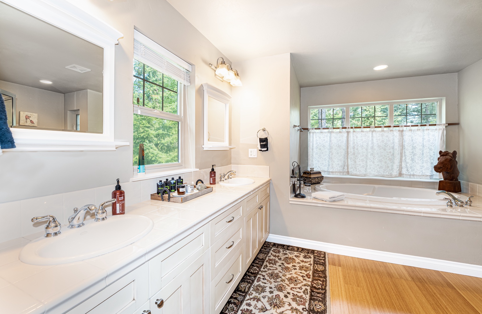 Soak your cares away in the bright, spacious bathroom with dual vanities, a deep soaking tub, and peaceful garden views through large windows.