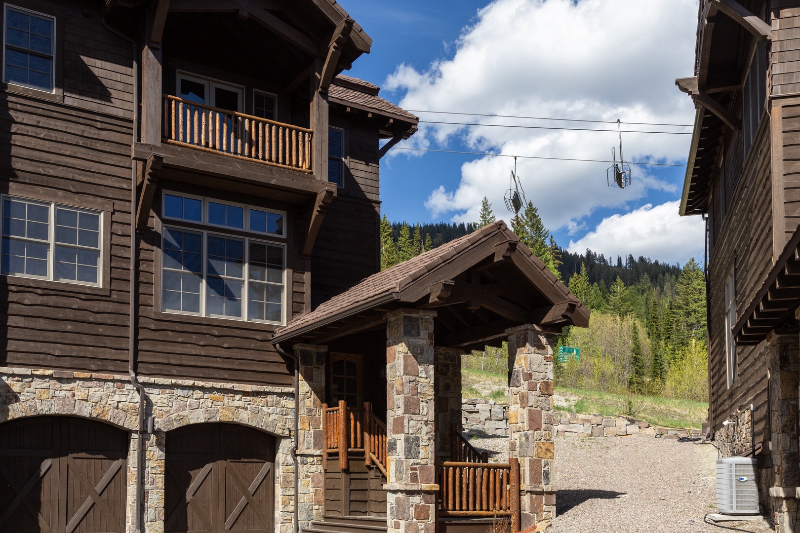 Private mountain retreat featuring rustic timber architecture, stonework, and balconies, nestled among evergreens under a clear blue sky.
