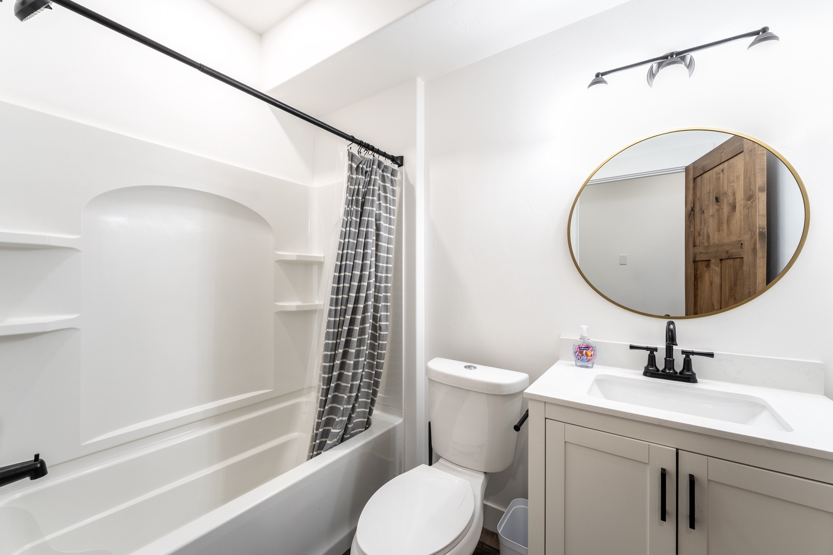 Refresh in your pristine bathroom with a relaxing tub-shower combo, stylish vanity, and elegant gold-rimmed mirror.