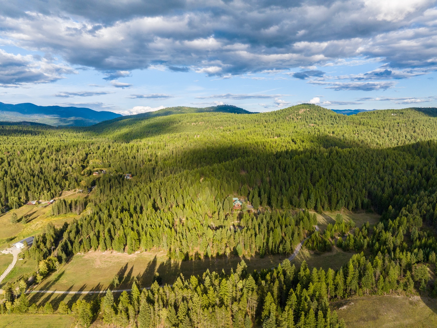Expansive aerial view showcases rolling forested mountains and scattered rural buildings nestled in valleys under dramatic cloudy skies.