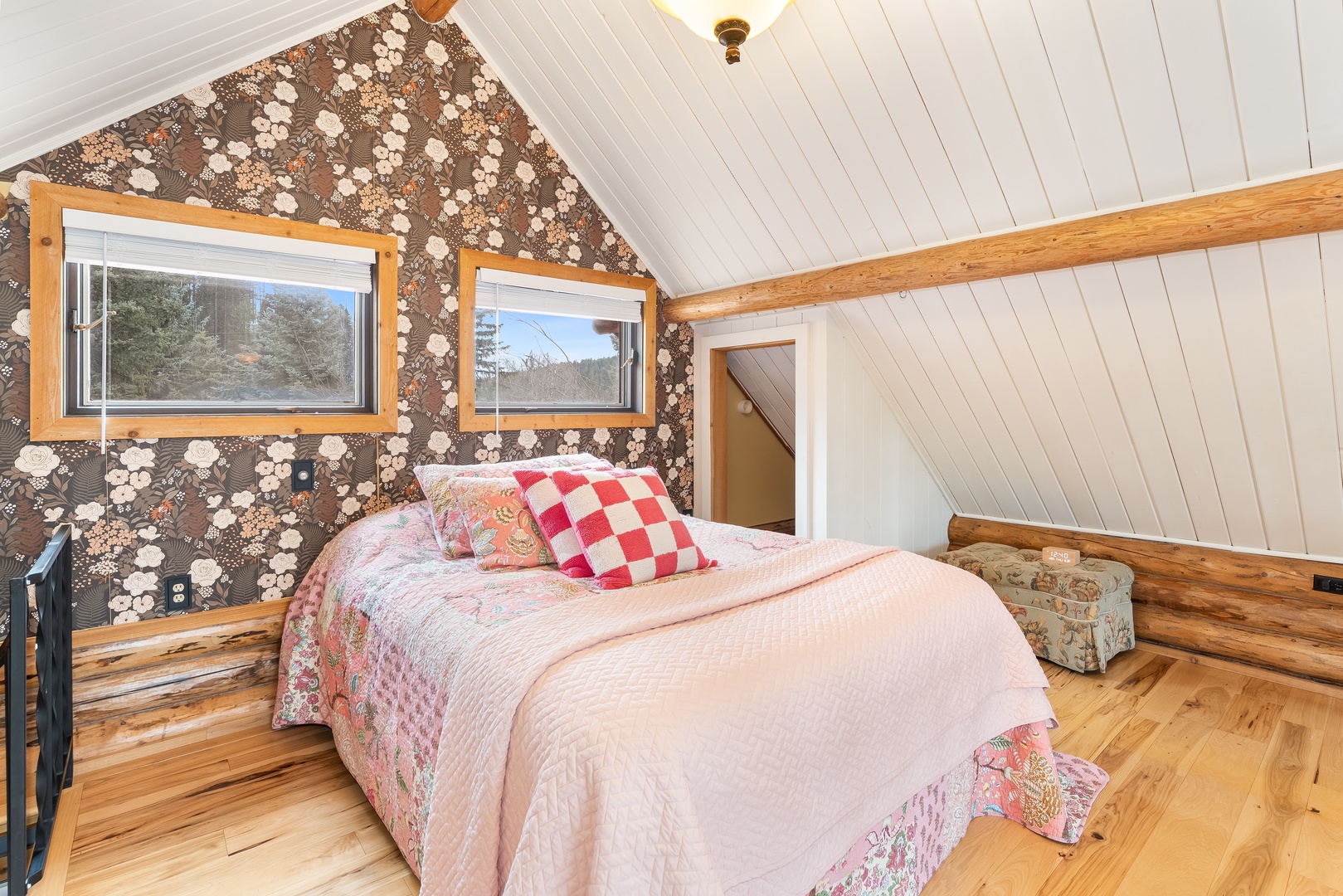 Cozy loft bedroom with charming floral wallpaper and soft quilted bedding where you'll drift off peacefully under sloped ceilings.