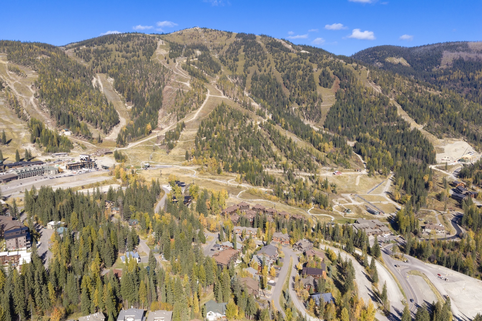 Aerial view of a mountain resort community nestled among forested slopes, with ski trails and lodges visible throughout the scenic alpine landscape.