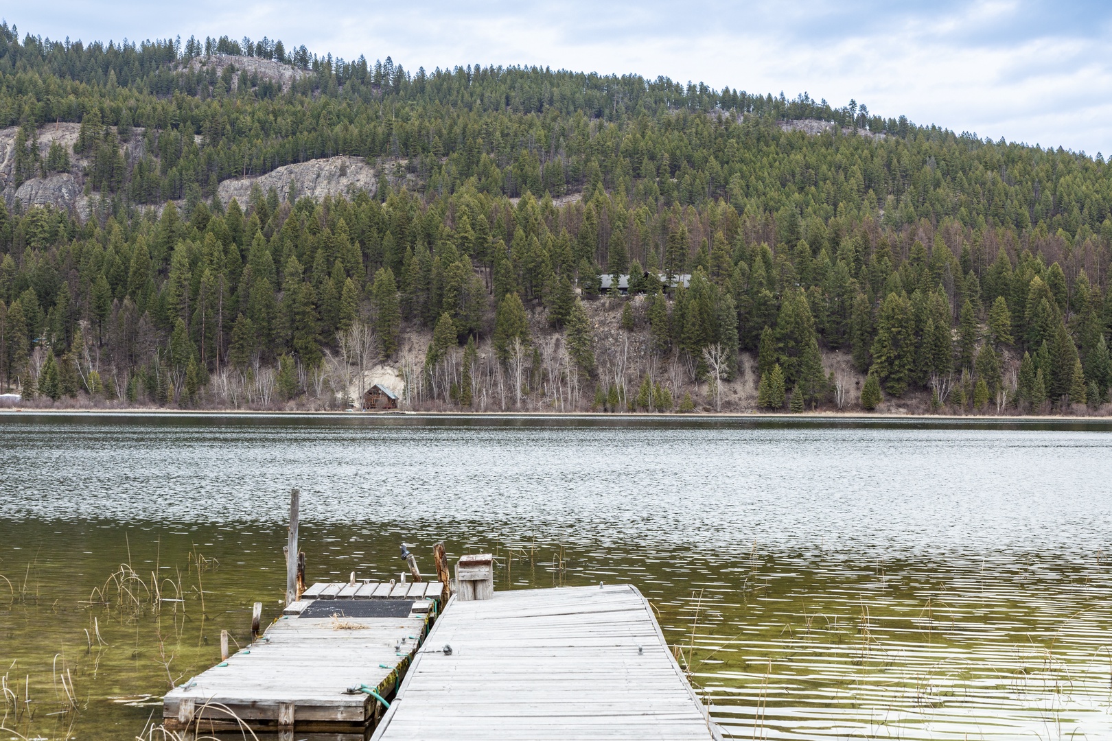Peaceful lakeside setting with forested mountains and private dock offering tranquil waterfront access.