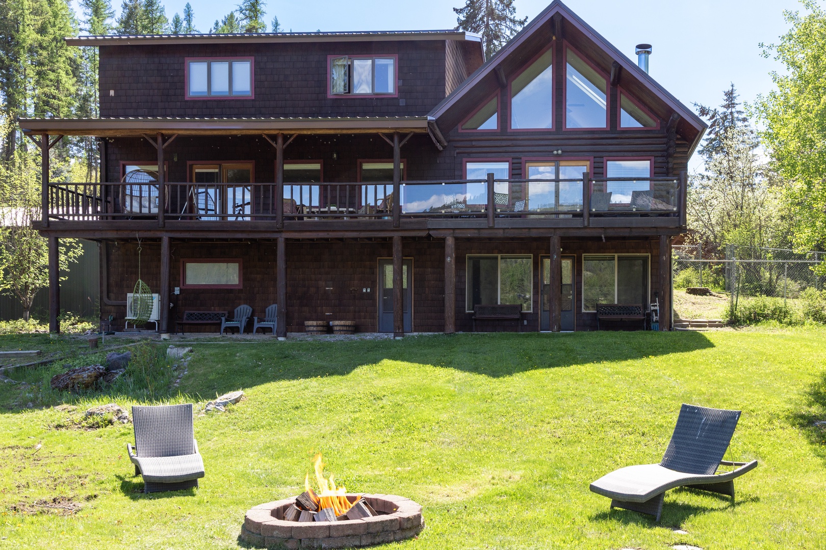 This stunning three-level lodge features a spacious deck, expansive windows, and a large lawn with a stone fire pit—perfect for gatherings. Surrounded by towering pines, it offers a peaceful, natural retreat in every season.