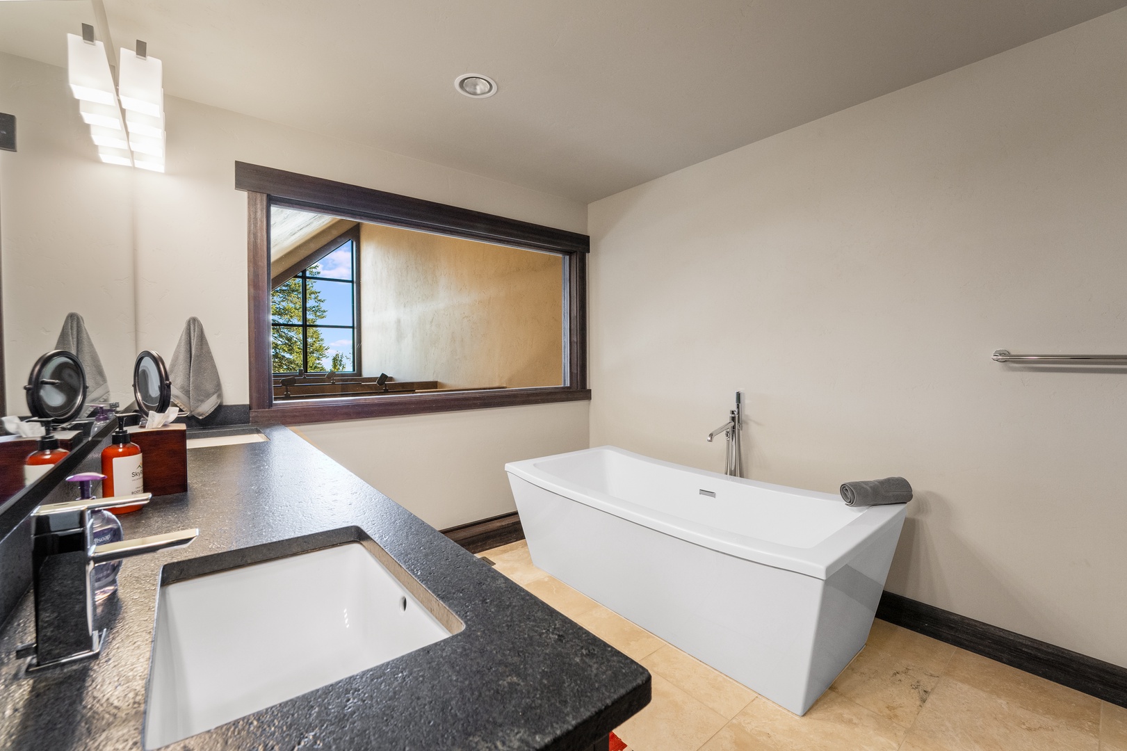 Unwind in your sleek, modern bathroom featuring a deep soaking tub and elegant finishes. Natural light pours through the window, creating a serene retreat where you can relax and recharge.