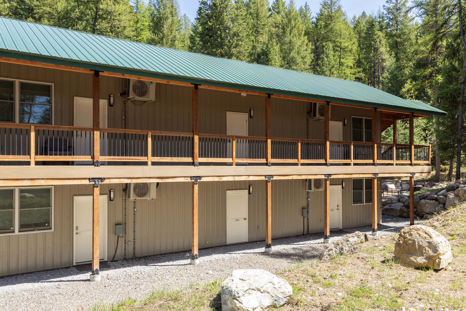 This modern two-story lodge nestled in a peaceful forest setting features covered balconies and a green metal roof, offering you a tranquil mountain retreat surrounded by towering evergreens.